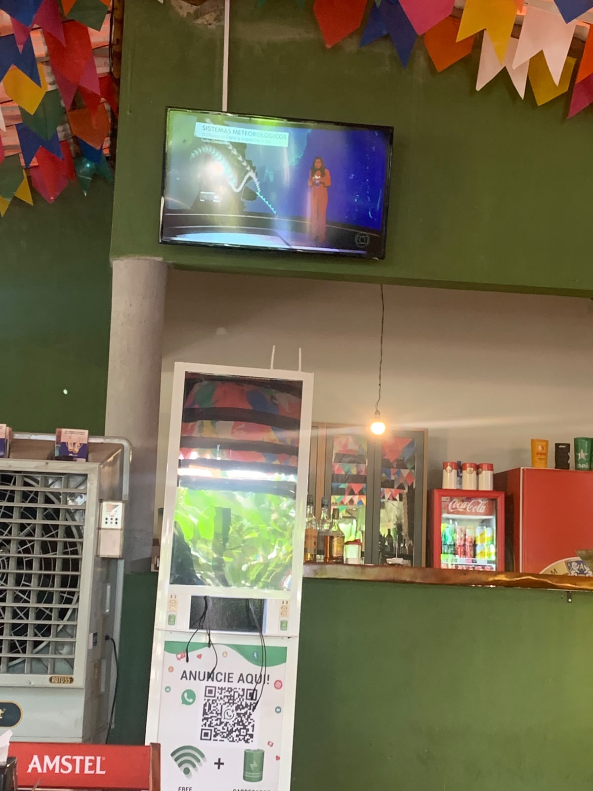 TV de bar passando o jornal da Globo, com um tótem caseiro de 'anuncie aqui' embaixo.