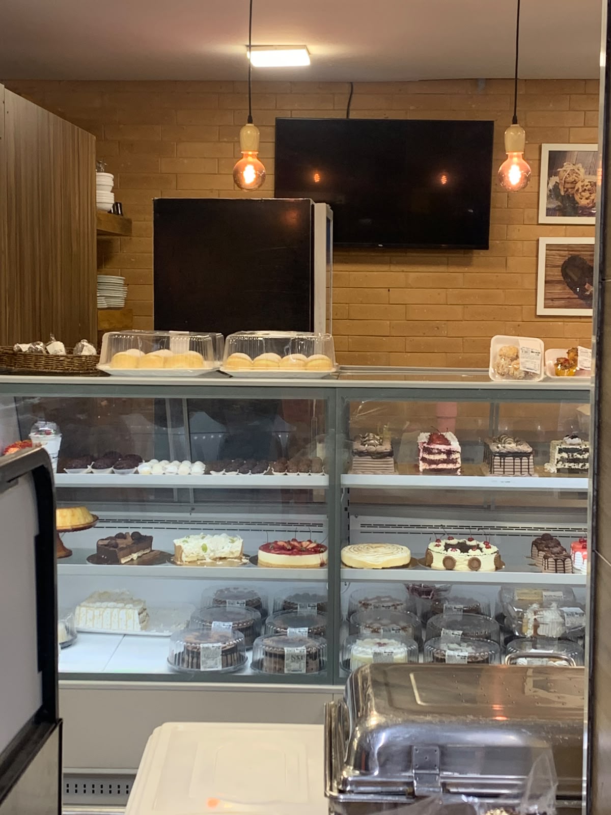 TV desligada na parede de uma confeitaria, logo acima do balcão de bolos.