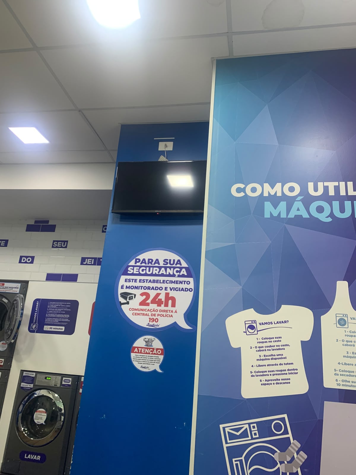 TV desligada pendurada numa coluna de lavanderia, em cima do painel de instruções.