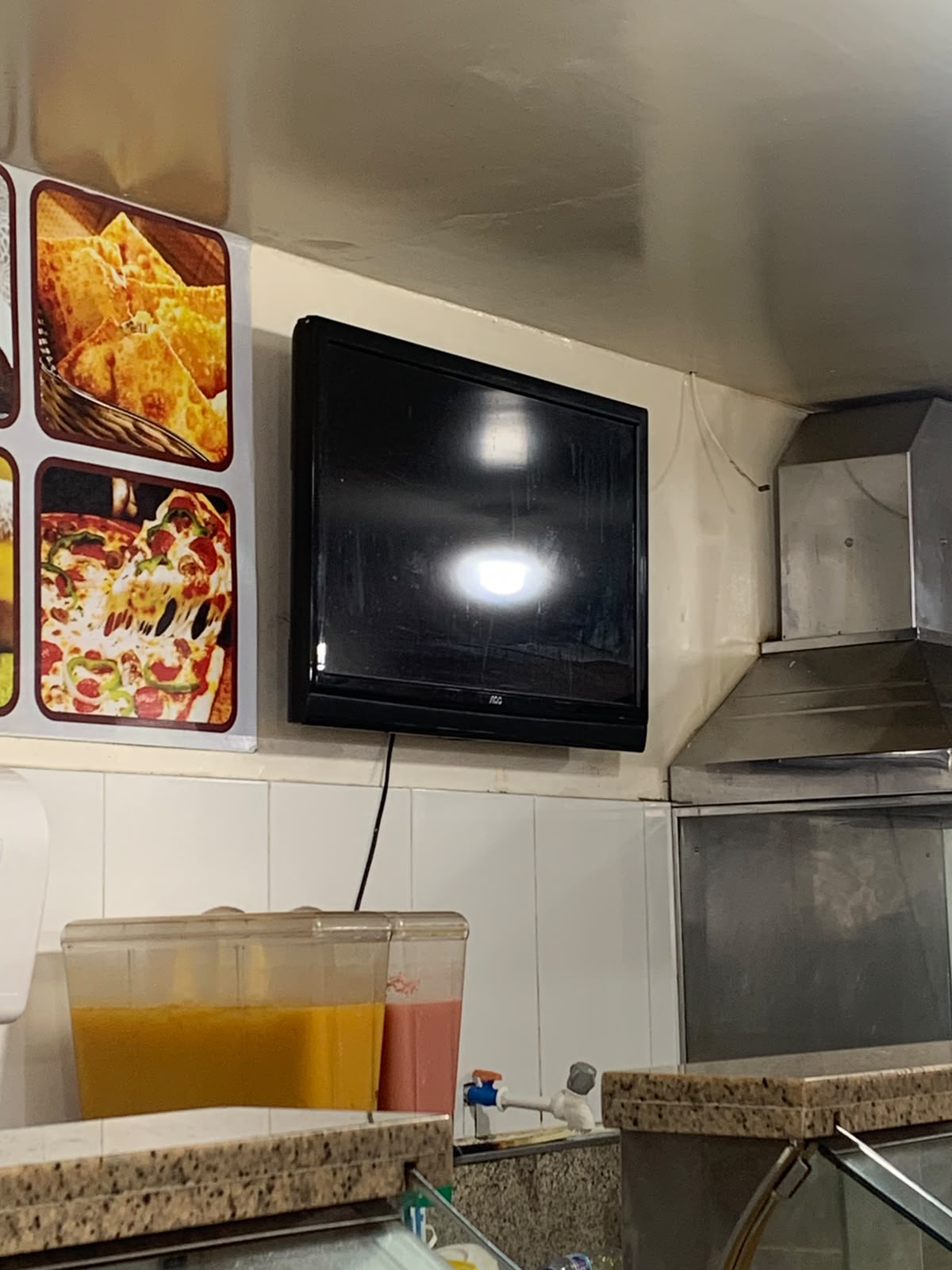 TV antiga desligada numa pizzaria, ao lado dos sucos do balcão.