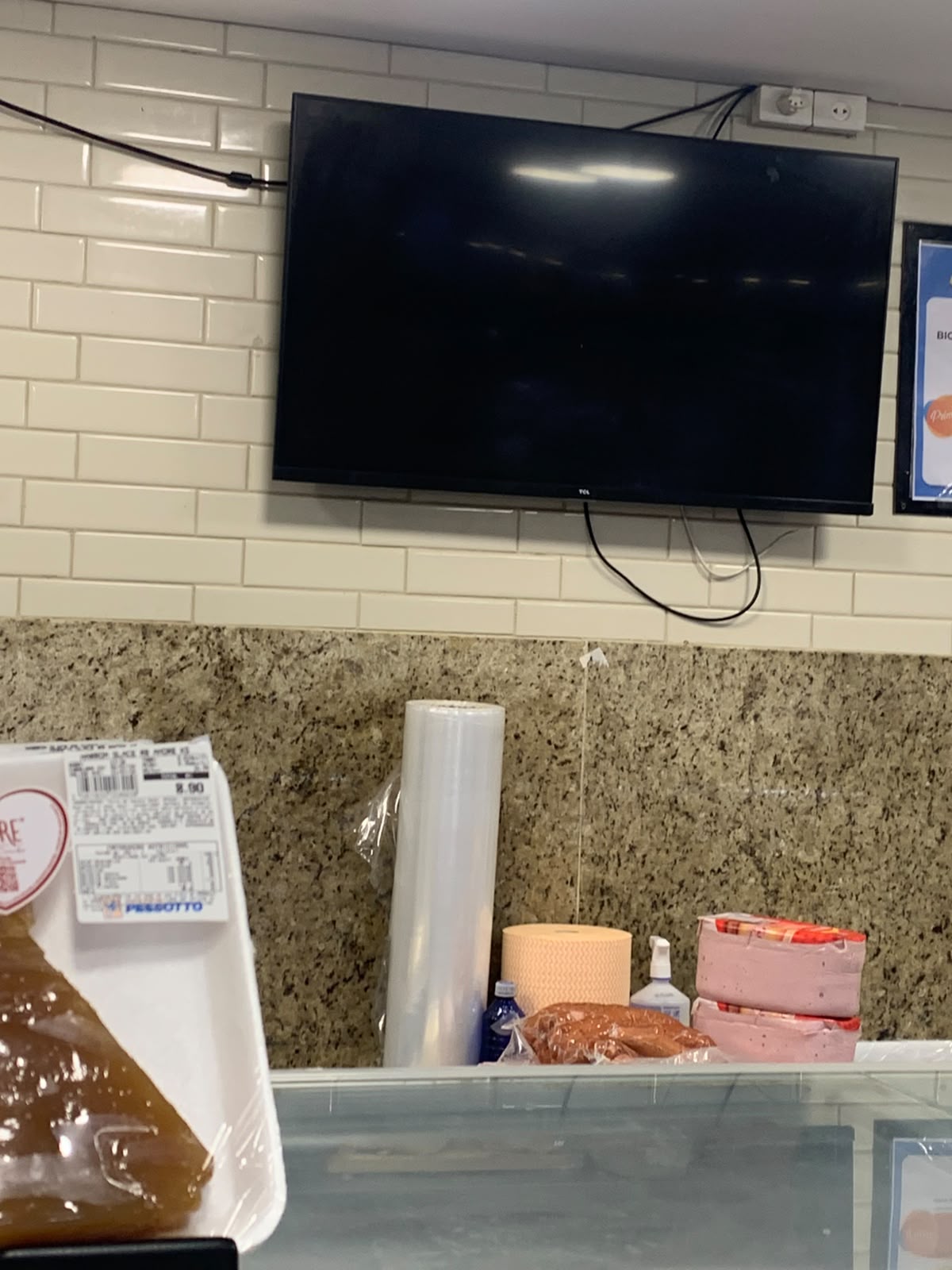 TV grande e desligada em cima do balcão de frios de um mercado.